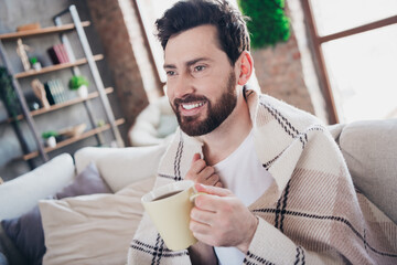 Photo of attractive man wrapped plaid sitting on couch relax rest quarantine treatment drink hot...