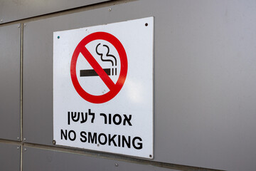 A warning sign with the inscription No smoking in Hebrew and English hangs on a wall outside