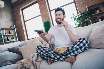 Photo of attractive bearded young man in pajamas enjoying weekend at home watching movie living...