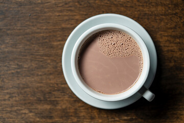 White cup with cocoa drink on wooden background, closeup, copy space, top view. Trendy healthy drink