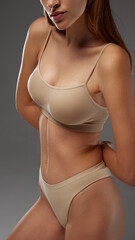 Model in beige underwear shows confident pose, focusing on toned upper body and posture against warm grey background. Concept of female health dieting, natural beauty, wellness. Ad