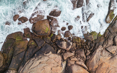 Aerial View of Waves Crashing Against Rocky Shoreline, Capturing Natural Coastal Patterns