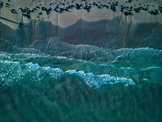 Aerial view of gentle ocean waves rolling onto a sandy beach, with soft turquoise waters creating...