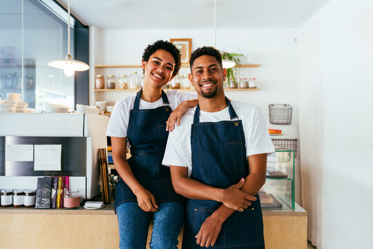 Bakery, happy portrait of hispanic black man and woman in cafe ready for serving pastry, coffee and baked foods - Confident waiter barista by counter for service, help and welcome in a coffee shop - Powered by Adobe