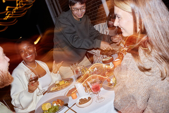 Distorted image of multiethnic group people enjoying late night party together at dinner table outdoors with light effects