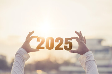 A man's hand holds the numbers 2025 against a city background.