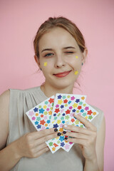 Portrait of young Caucasian woman winking at camera while holding sheets of colorful star-shaped...