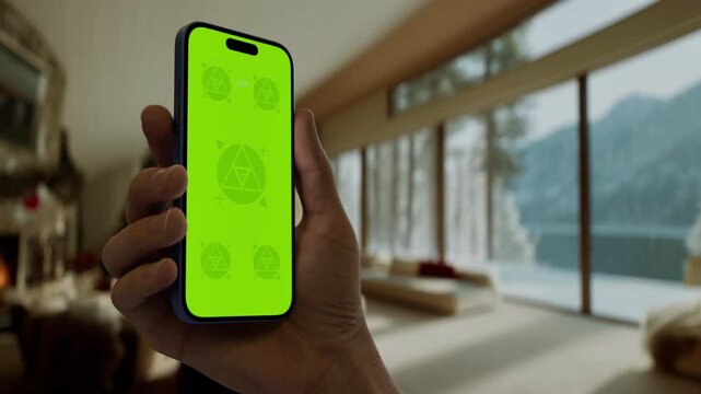 GREEN SCREEN CHROMA KEY A hand holding a smartphone in a cozy living room with a festive Christmas setting. Perfect mockup for holiday shopping, or festive apps
