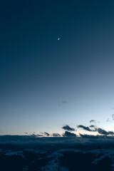 Crescent moon over snowy mountains during twilight in a serene winter eveningv