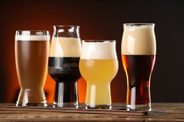Glasses with different types of beer on wooden table against color background
