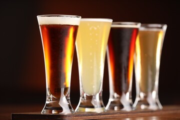 Glasses with different types of beer on wooden table against color background, closeup