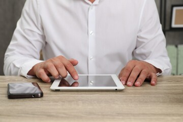 Businessman with tablet and smartphone at wooden table, closeup. Modern technology