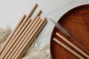 Bamboo drinking straws and cleaning brush on marble table, top view