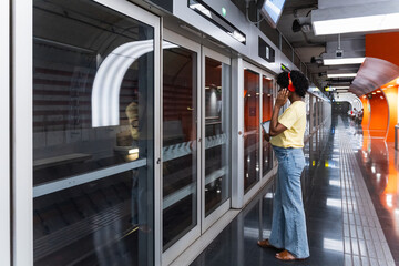 Young woman standing in front of subway at platform while listening music