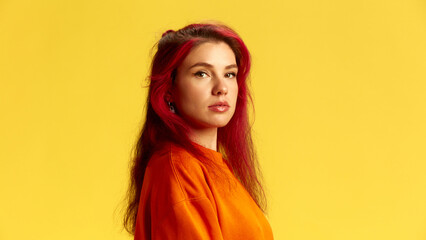 Side view portrait of young serious woman looking at camera, deep in thought, wearing vibrant orange outfit. Confidence. Concept of human emotions, facial expression, lifestyle