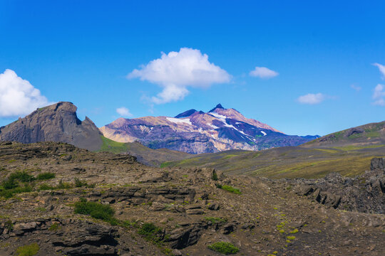 Scenic view on snow covered peak of Ymir with Rhino shape rock on left and scenic volcanic icelandic nature during beautiful day and blue sky with clouds when hiking Laugavegur trail near Thorsmork