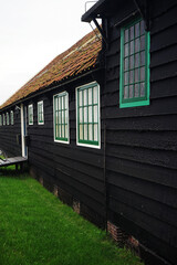 Old wooden house with black walls and green windows in gloomy weather
