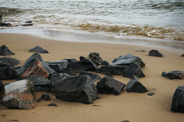 Obraz premium Sandy beach with large black stones in non-sunny weather