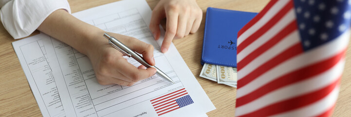 Young woman fills in visa application form near USA flag