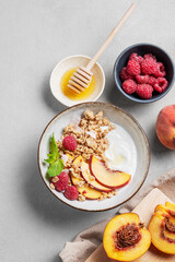 Flat lay of greek natural yogurt with oat granola or muesli, peach, raspberry and honey in a bowl...