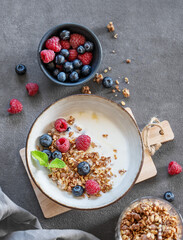 Granola with greek yogurt, raspberries and blueberries in a bowl on a wooden board on a dark background