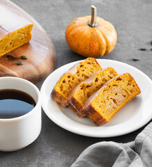 Pumpkin sweet bread or cake with icing on a plate on a dark background with decorative pumpkins and a cup of  coffee.