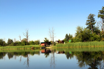 Fototapeta premium Charming houses lined along a riverbank with lush greenery under clear blue sky and gentle ripples on water