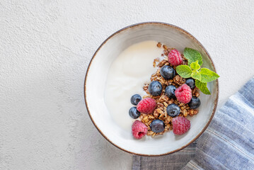 Granola with greek yogurt, raspberries and blueberries in a bowl on a white background with napkin.