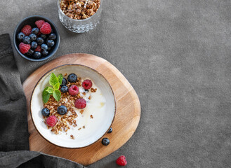 Granola with greek yogurt, raspberries and blueberries in a bowl on a wooden board on a dark background