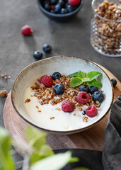 Granola with greek yogurt, raspberries and blueberries in a bowl on a dark background with fresh berries and leaves.
