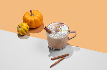 Spice pumpkin latte in glass cup on orange background with decorative pumpkins, cinnamon sticks and shadows.