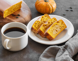 Pumpkin sweet bread or cake with icing on a plate on a dark background with decorative pumpkins and a cup of  coffee.
