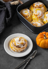 Pumpkin rolls with creamy glaze and cinnamon on a plate on a dark  background.