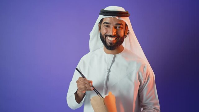 Handsome saudi arabian middle-eastern man with traditional thwab portrait in studio on colored backgrounds and gel colored lights.	
