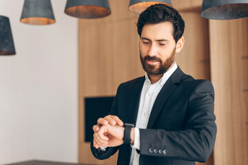 Pensive attractive man, businessman wearing suit looks at the clock, late working in modern office