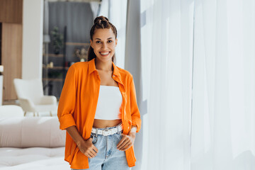 Attractive, smiling Hispanic woman wearing stylish yellow shirt, looking at camera, posing at home