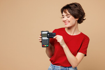 Young happy woman wear red t-shirt casual clothes hold wireless modern bank payment terminal to...