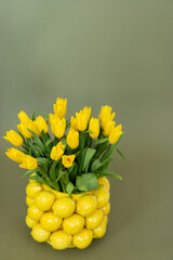 A creative floral arrangement of vibrant yellow tulips styled in a charming lemon-shaped vase against a soft green backdrop