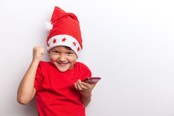 a boy in a Santa costume holds a smartphone in his hands. an emotional little santa. a cheerful child for Christmas with a phone.