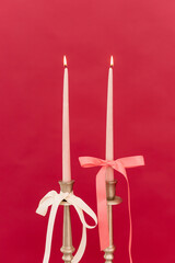 Elegant candles adorned with pastel ribbons glowing softly against a vibrant red backdrop, creating a romantic atmosphere