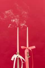Delicate pink candles gently flicker with wisps of smoke against a vibrant red backdrop, creating a...