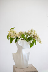 A stunning white vase shaped like a bust, filled with delicate flowers against a minimalistic wall backdrop
