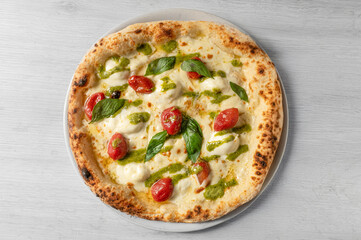 Italian pizza with buffalo mozzarella, confit, basil pesto and pine nuts, fresh basil, from above on white wooden background