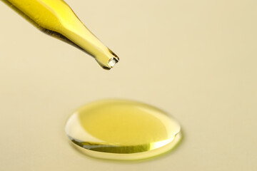 Cosmetic oil dripping from pipette on dark beige background, closeup. Space for text