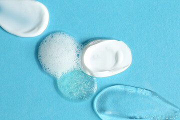 Smears of different cosmetic products on light blue background, top view