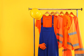 Workers' uniforms on clothing rack against yellow background. Space for text