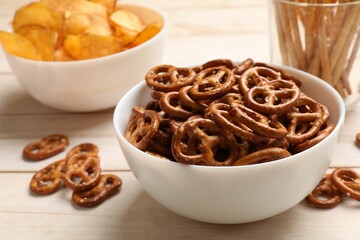 Delicious pretzel crackers and other snacks on white wooden table, closeup