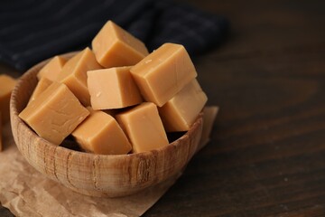 Tasty sweet caramel candies in bowl on wooden table, closeup. Space for text