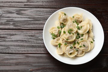 Delicious pelmeni with green onion on wooden table, top view. Space for text