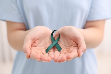 Woman with teal ribbon on light background, closeup. Ovarian cancer and gynecological disorders awareness